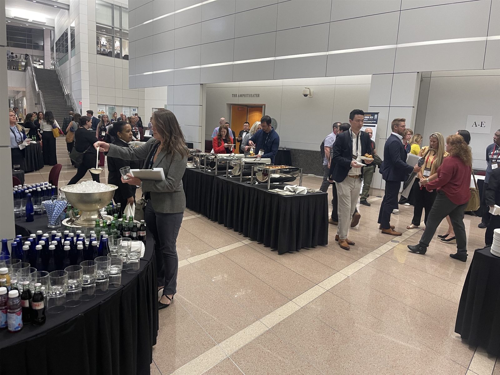 Badge-wearing guests moving through a buffet and beverage station in a marble-floored conference atrium
